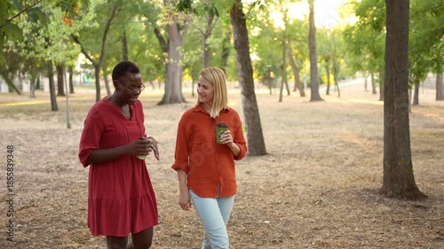 Two multiracial female friends walking and talking in a park