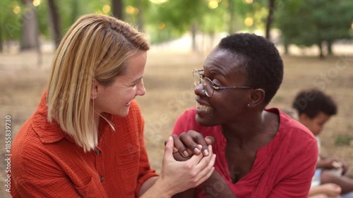 Two multiracial women friends talking, laughing and hugging in a park