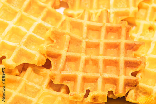 Waffles overlap in crisp, appetizing stack, their grid pattern catching warm light. Texture and color suggest freshly made perfect for a cozy breakfast or food styling
