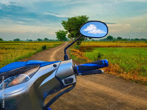 Right rear mirror, handlebars, brake system, and power hand switch motorcycle on a road between the rice fields.