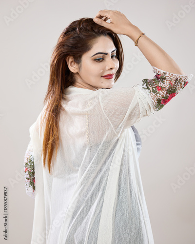 Elegant fashion portrait of a woman looking back over her shoulder with her hand placed on her head against a clean studio background. Modern outfit, graceful posture, and soft lighting convey confide