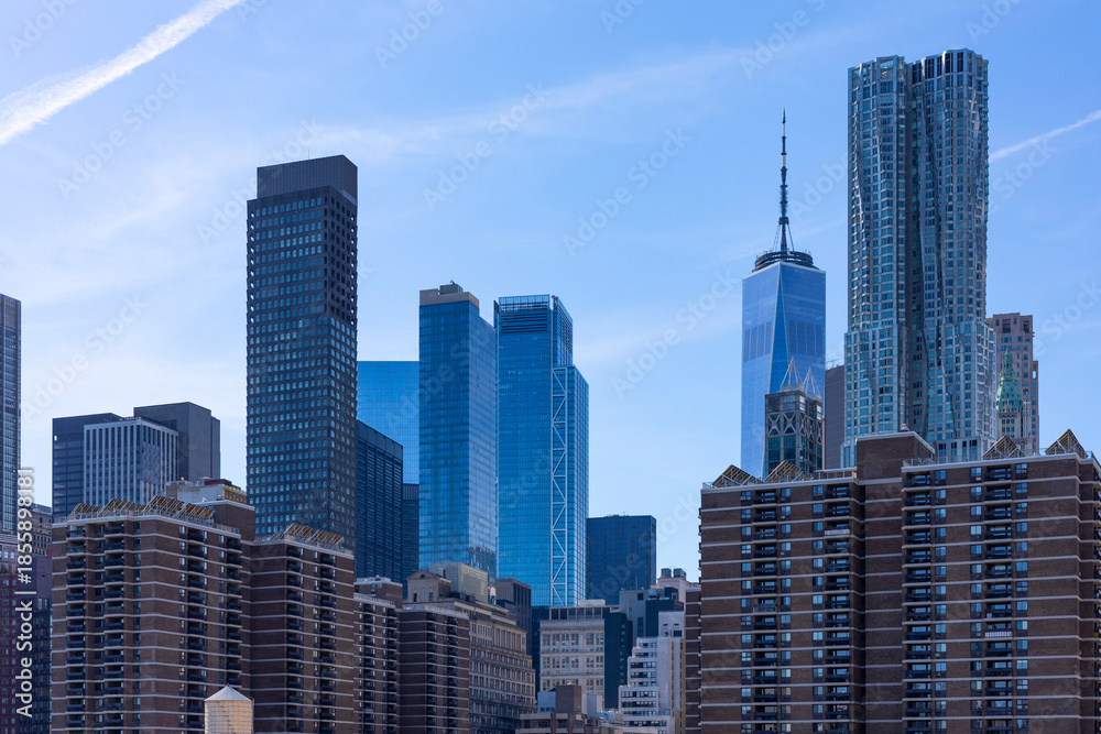 Fototapeta premium The Lower Manhattan skyline features One World Trade Center and glass skyscrapers rising behind brick residential apartment buildings in NYC.