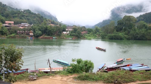 A serene summer landscape of wooden fishing boats on the calm water of a mountain lake with a reflection of the sky and clouds over the distant coast