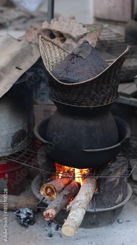Lao Sticky rice cooking style, a metal pot sits on an iron grill over a burning wood campfire, where hot flames and smoke cook a delicious meal in nature