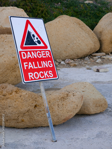 warning sign for falling rocks at coastal cliff with large boulder