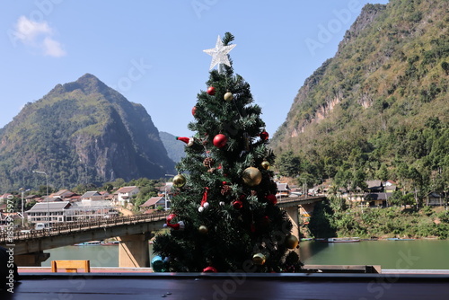 A big blue Christmas tree with a star ornament stands by a Barcelona temple on a bridge, featuring winter holiday lights and festive New Year decorations under a seasonal sky