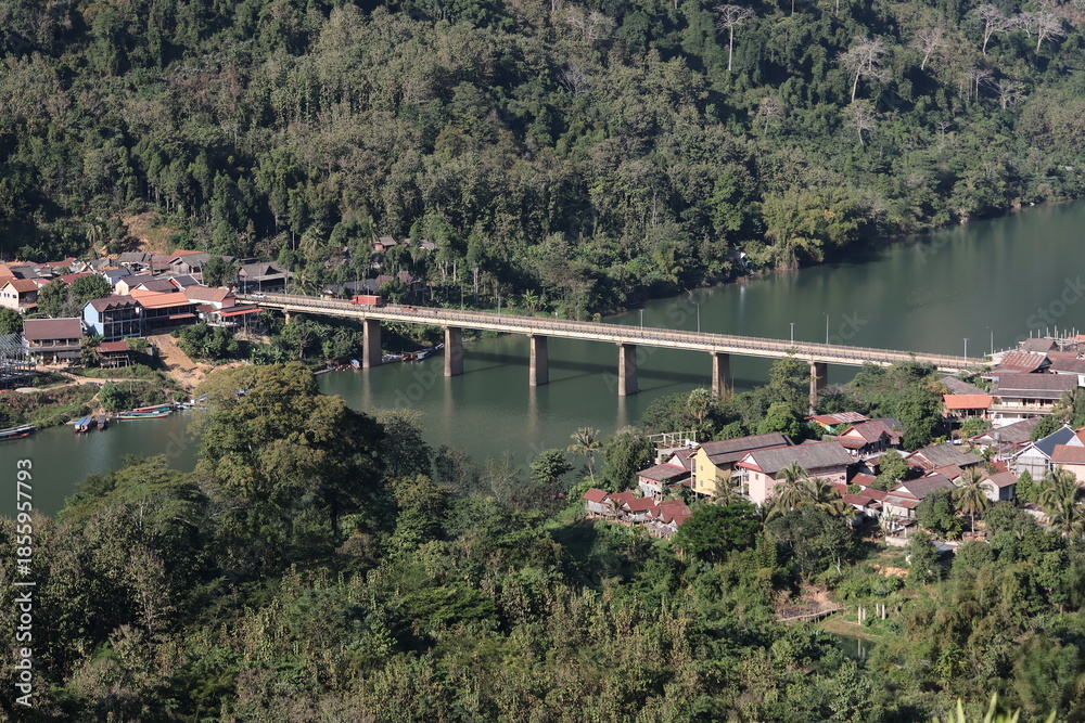 Obraz premium Panoramic autumn mountain landscape featuring a high peak view over a misty forest valley with green trees and a lake under a cloudy sky in Laos
