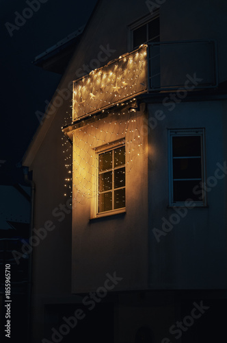 Hauswand mit beleuchtetem und dekorierten Fenster sowie Balkon