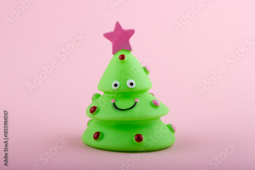 Small green toy Christmas tree with on pink background. Happy New Year concept.