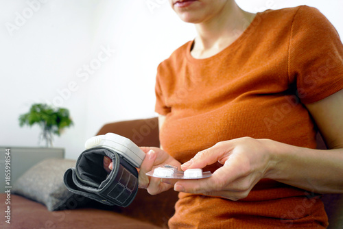 Obraz na plátně Woman holding a pill blister pack with a digital blood pressure cuff nearby in a domestic setting