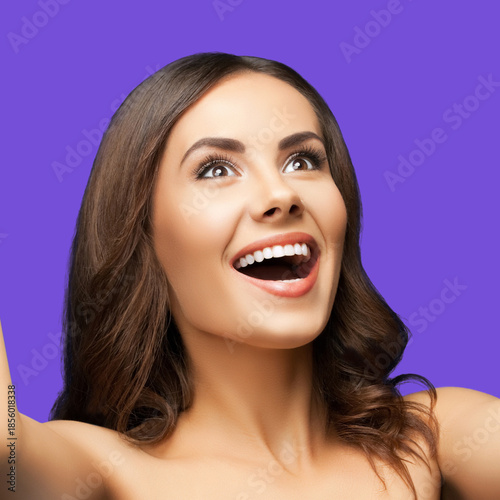 Portrait of very happy, expressive emotional looking up beautiful woman, isolated against violet purple color background. Cute joyful brunette girl at studio. Dental care ad. Square image
