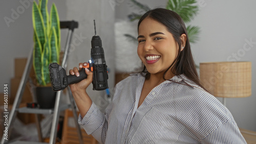 Φωτογραφία Woman holding drill smiling in modern living room with plants and ladder visible suggests home improvement in new house