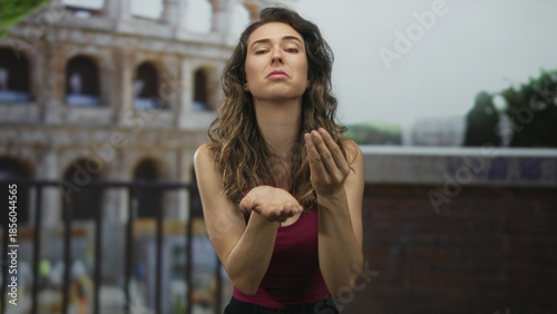 Fotografía Woman in pink tank top extends both open palms toward sunlit ancient roman coliseum building; desperation