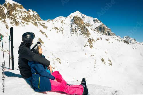 Young caucasian couple pose sits hug enjoying looking at snowy mountains in winter. Get away skiing holidays lifestyle. Tetnuldi ski resort viewpoint. Caucasus mountains high altitude freeriding
