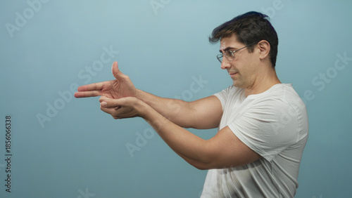Man pointing finger in a playful gun gesture with hands toward camera wearing white shirt in a studio; playful confidence.