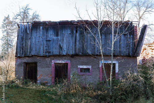 Old abandoned rural buildings. Decaying wooden door set in a cracked brick wall overgrown with plants. A symbol of passing time, neglect and forgotten places