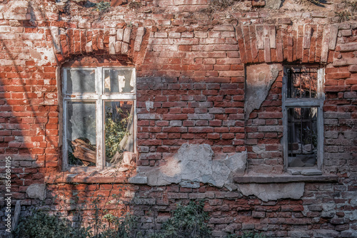 Old abandoned rural buildings. Decaying wooden door set in a cracked brick wall overgrown with plants. A symbol of passing time, neglect and forgotten places