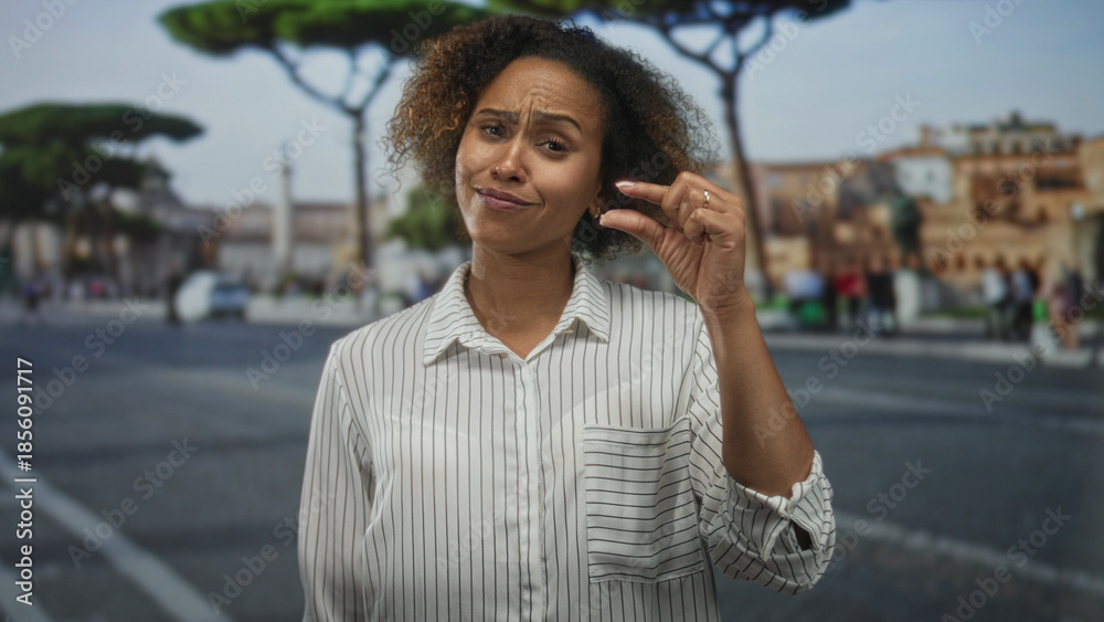 Fototapeta premium Woman smiling, holding small object between fingers and showing hand in striped shirt on street; optimism travel discovery.