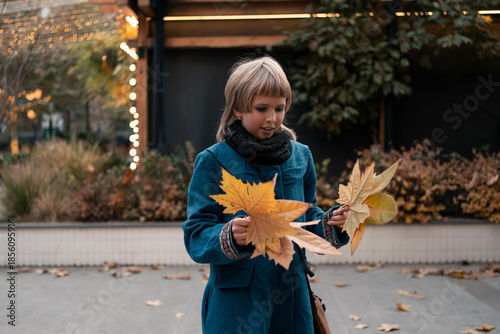 Teenage girl at walk in autumn city collecting platan golden leaves