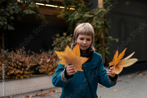 Teenage girl at walk in autumn city collecting platan golden leaves