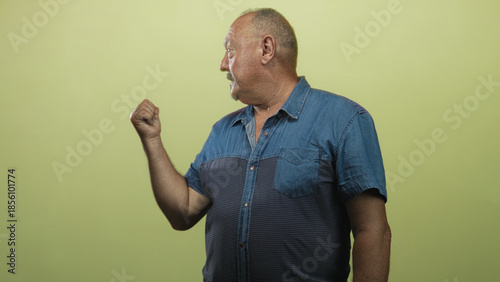 Tableau sur toile Senior hispanic man in denim shirt clenching fist and looking sideways in studio; determination resilience dignity