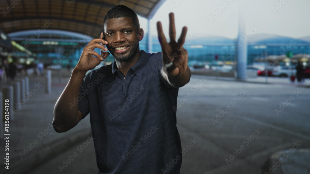 Fototapeta premium Man talking on phone, smiling and holding smartphone with palm extended toward camera at airport curb; confidence connection.