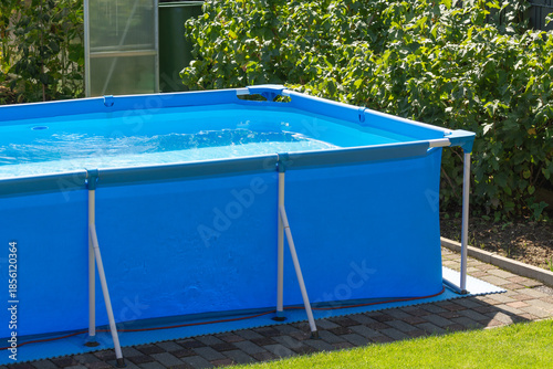 A close-up shot of the clear water swimming pool in the backyard. A beautiful garden with a greenhouse and various plants provides a relaxing area for the whole family during the summer heat.