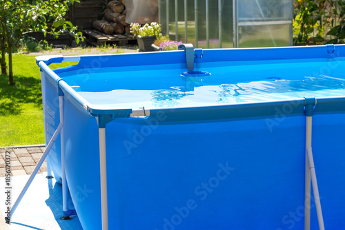 A close-up shot of the clear water swimming pool in the backyard. A beautiful garden with a greenhouse and various plants provides a relaxing area for the whole family during the summer heat.