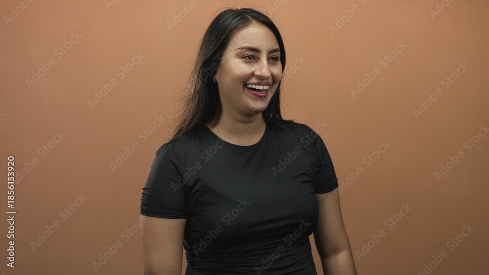 Obraz premium Woman laughing with open mouth and visible teeth in a studio with peach backdrop wearing black shirt; joy confidence.