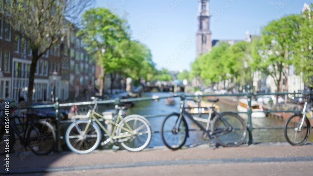 Fototapeta premium Blurred bicycles against the scenic amsterdam canal backdrop, showcasing the charm of the netherlands with a defocused city view and vibrant bokeh enhancing the urban appeal.