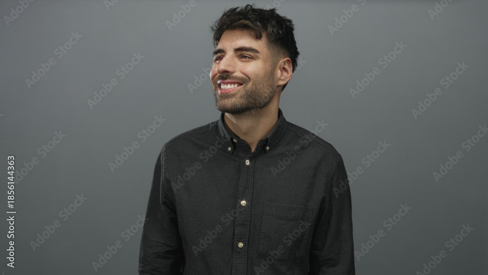 Obraz premium Man wearing casual buttondown shirt looking up and smiling against grey studio wall; optimism growth ambition.