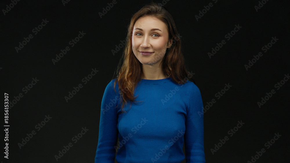 © Krakenimages.com - Young woman smiling against isolated black background embodying confidence and serenity in casual blue sweater with long hair © Krakenimages.com - Young woman smiling against isolated black background embodying confidence and serenity in casual blue sweater with long hair