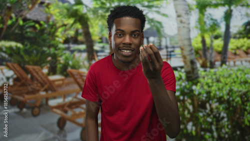 Young african american man in a red shirt beckons with a hand in a forest clearing; welcoming invitation.