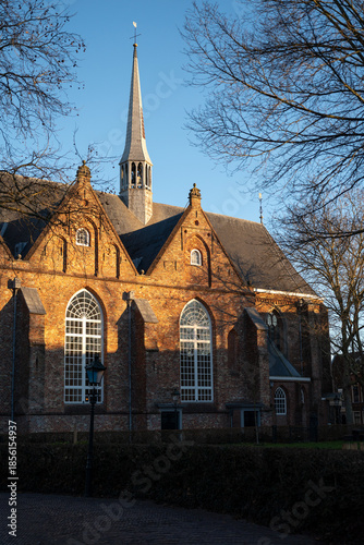 Sunlit close-up of the Jacobijnerkerk, also known as the Grote Kerk, in Leeuwarden, the Netherlands. Warm sunlight highlights the brick facade and architectural details.