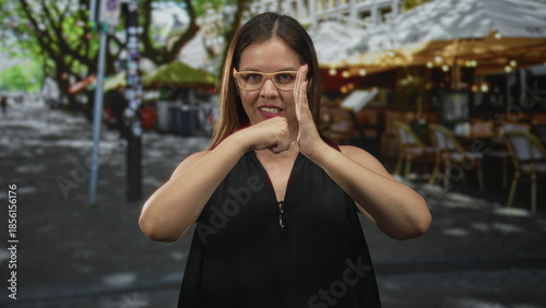 Schilderij op canvas Woman wearing glasses making fist to palm gesture with visible hands on street terrace cafe outdoors; strength determination