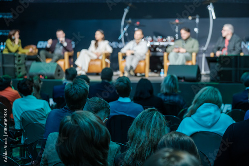 Wallpaper Mural Panel discussion on stage with diverse speakers and attentive audience. Conference atmosphere with live talk and engaged crowd. Audience sits in rows watching panel lights highlight participants  Torontodigital.ca