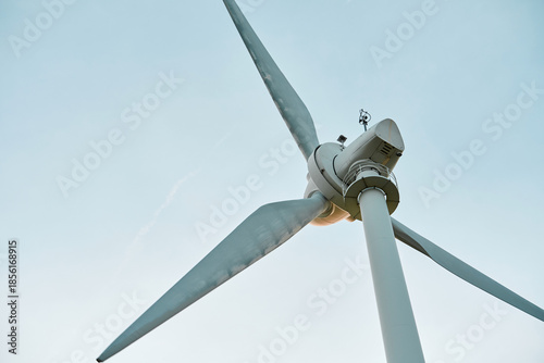 Wind turbine against clear sky. Modern three-blade turbine with platform and equipment atop the tower.