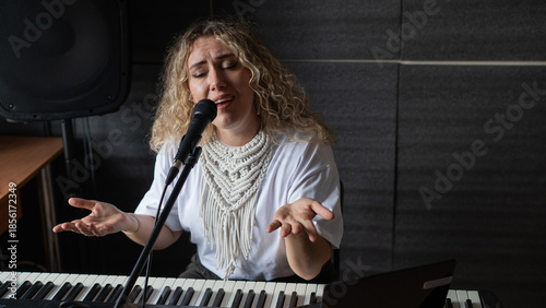 Caucasian woman singing into microphone and recording herself on laptop. 