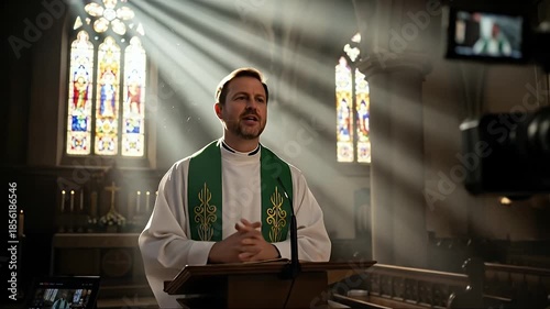 A priest delivers a sermon in a church with a camera recording the service.