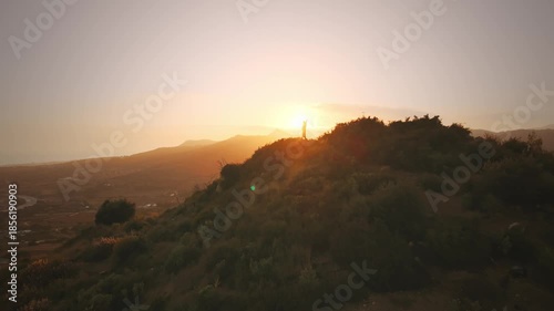 A person is standing on a hill with a beautiful sunset in the background. The person is smiling and he is happy