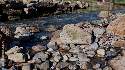 Flowing stream water moving between rocks and pebbles near the beach in Ericeira, Portugal. Natural movement of water with scattered stones, organic debris and coastal textures