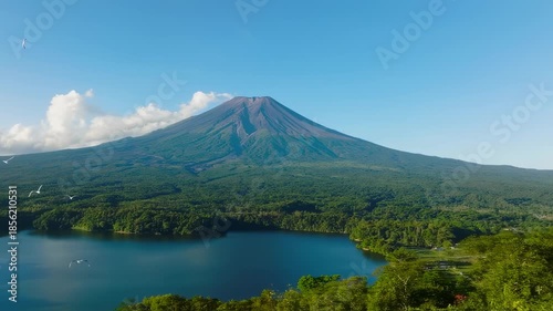 A serene mountain rises over a lake, with birds in flight, trees surrounding the water