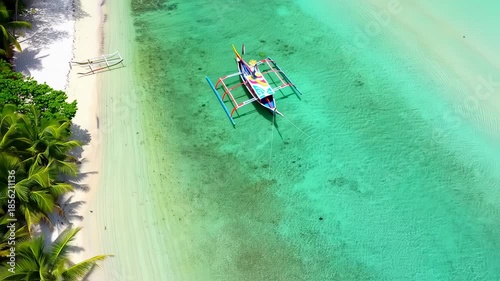 Aerial view of a tropical beach with turquoise water and a colorful outrigger boat