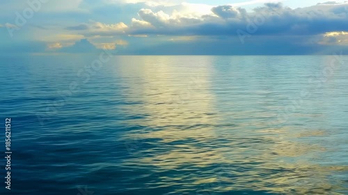Calm seascape showing a rippled ocean surface under a sky with sunlit clouds