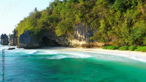 Scenic coastal view of a cove with lush greenery, rocky formations, sandy beach, and turquoise water