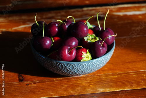 Delicious fresh cherries and strawberries sit in a bowl on a wooden table