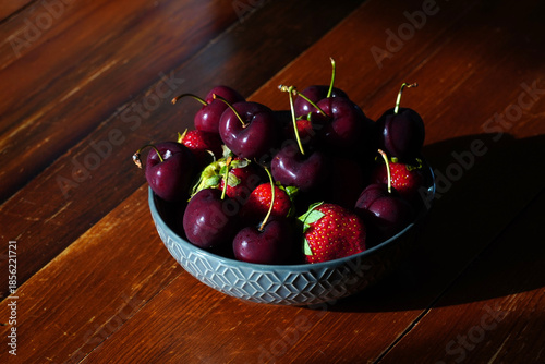 Delicious fresh cherries and strawberries sit in a bowl on a wooden table