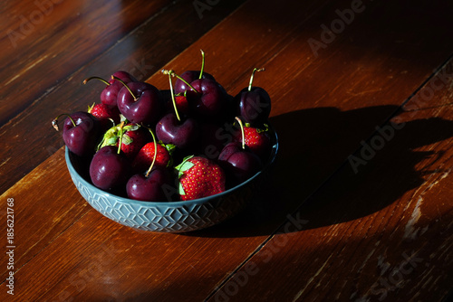 Delicious fresh cherries and strawberries sit in a bowl on a wooden table