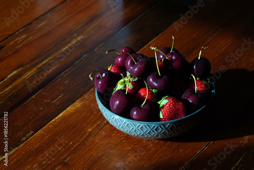 Delicious fresh cherries and strawberries sit in a bowl on a wooden table