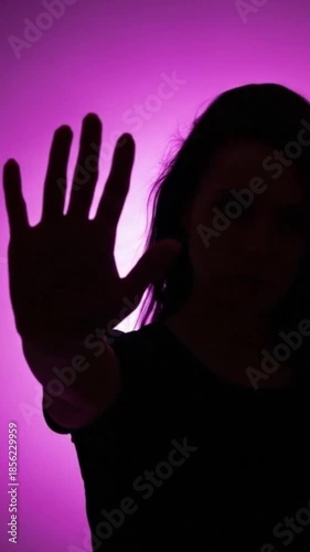 Silhouette of a person holding up their hand in a stop gesture against a pink background. Say no to violence against women, femicide.
